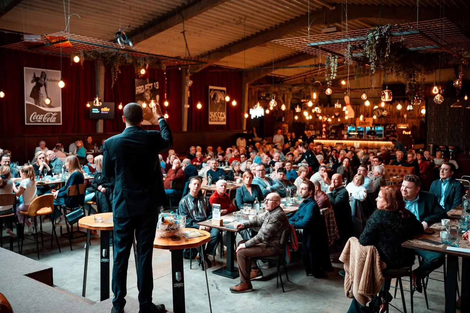 Speaker addressing a packed, warmly lit venue